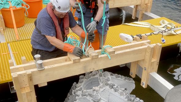 Två arbetare lastar ombord en betongklump på en pråm.