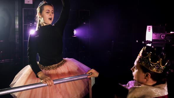 En person i tiara dansar, en annan person i kungakrona tittar på.