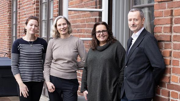 fyra personer står utanför en röd tegelbyggnad