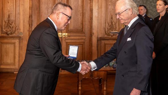 Professor Bengt Kristensson Uggla håller ask med medalj och skakar hand med H.M. Konungen i en sal på Kungliga slottet.