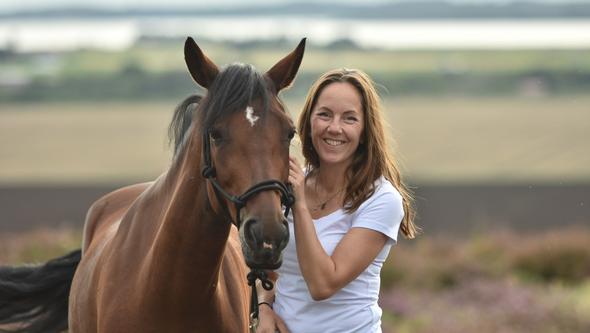 Linda Björkgren barnmorska står med en häst i ett öppet landskap 