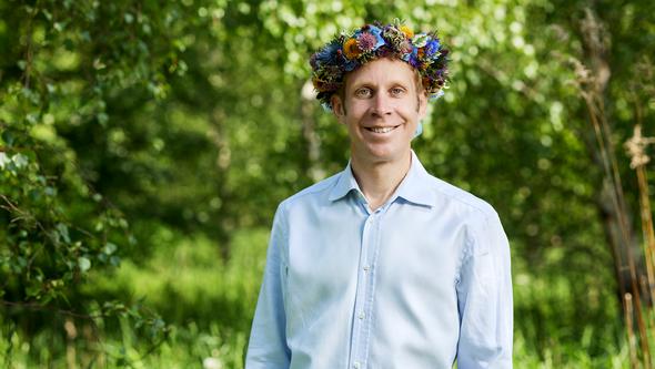 Man i skjorta i grönska med blomsterkrans på huvudet