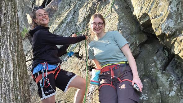 Izabella standing against a rock with a friend in climbing gear. 