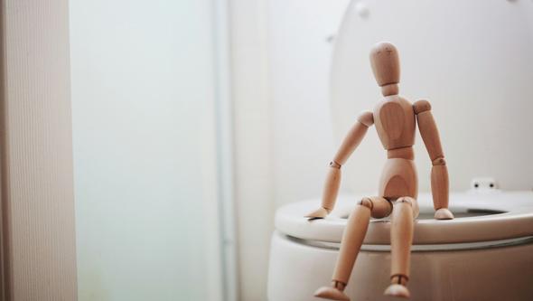 Wooden figure sitting on the toilet