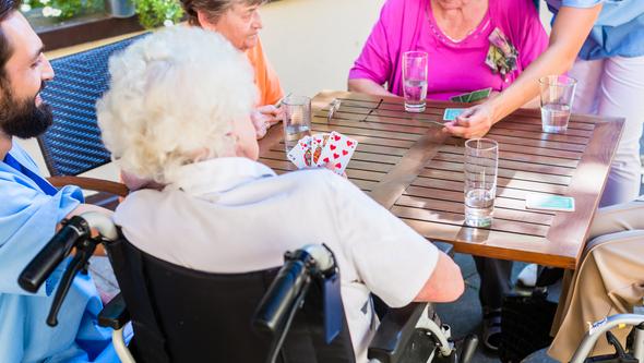 Seniorer och sköterskor spelar kort 