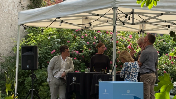 Paneldeltagarna står bakom ett ståbord under ett tält i en trädgård.