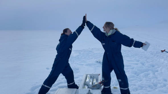 Two female researchers doing fieldwork on a glacier, giving each other a high five celebrating a successfull day at work