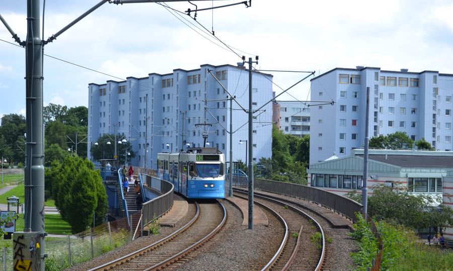 En spårvagn kommer genom Göteborg. I bakgrunden syns höghusbyggnader och grönskande träd i stadsdelen Biskopsgården i Göteborg. 