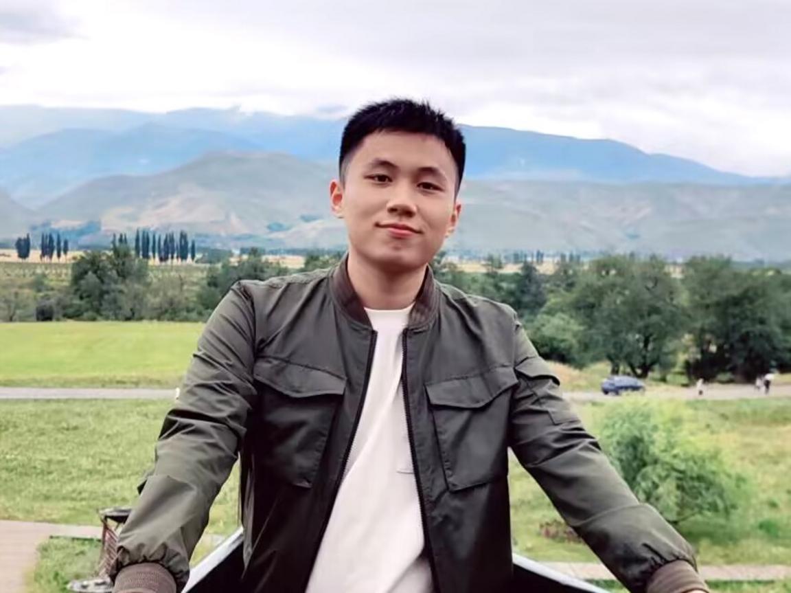 A PhD student in China in front of a mountain and green meadows