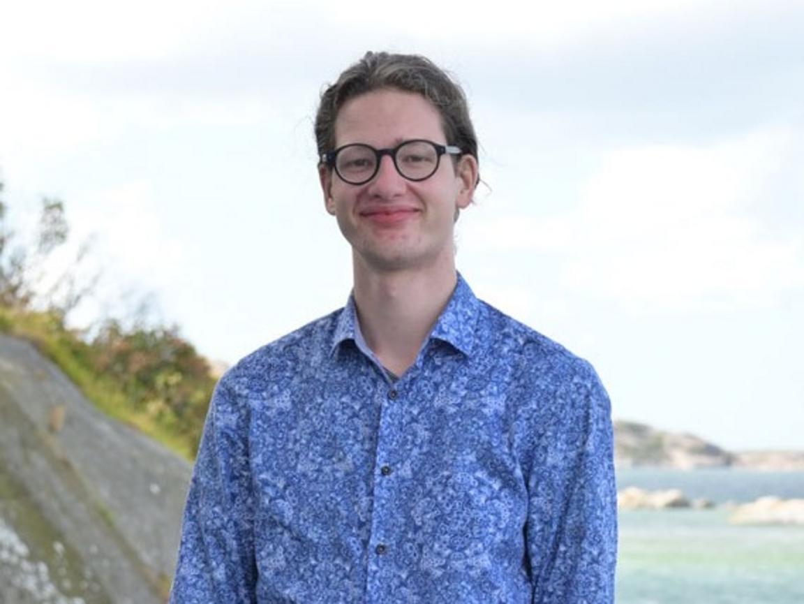 A portrait of a man who is standing on a dock in front of the ocean.