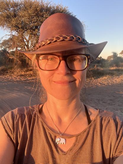 Woman with African bushveld behind in a brown leather hat